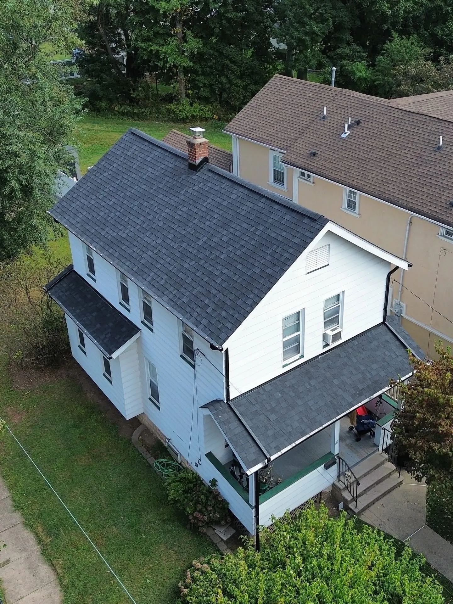 New black architectural shingle roof on a white two-story colonial with brick chimney and porch roof