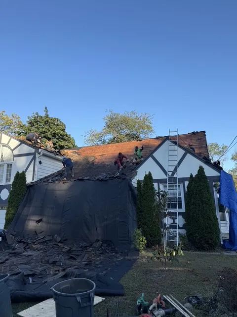 Full roof tear-off in progress on a Pompton Plains NJ Tudor home with debris tarps protecting landscaping