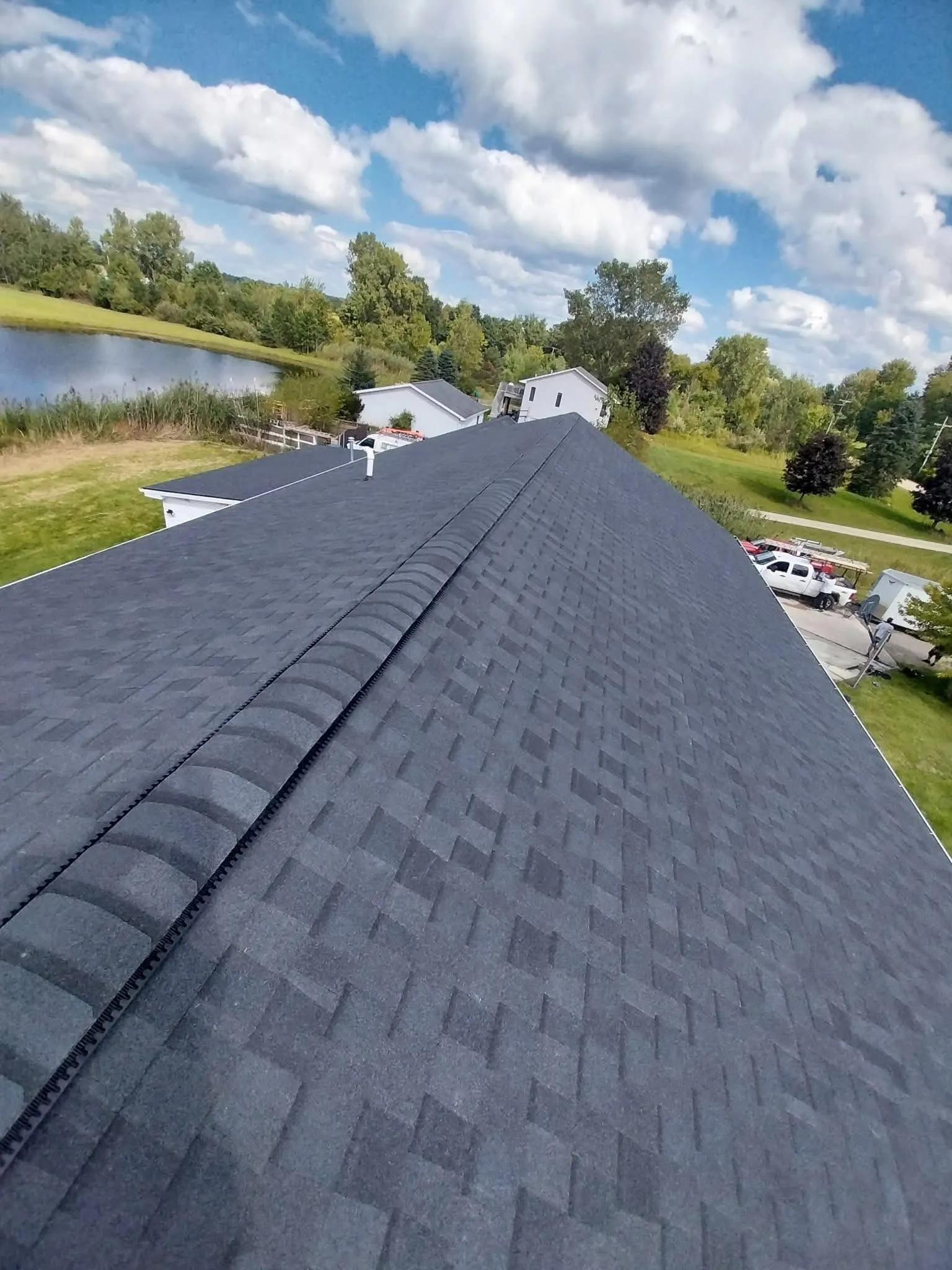 Ridge-line view of a completed charcoal shingle roof with continuous ridge vent, lake in the background