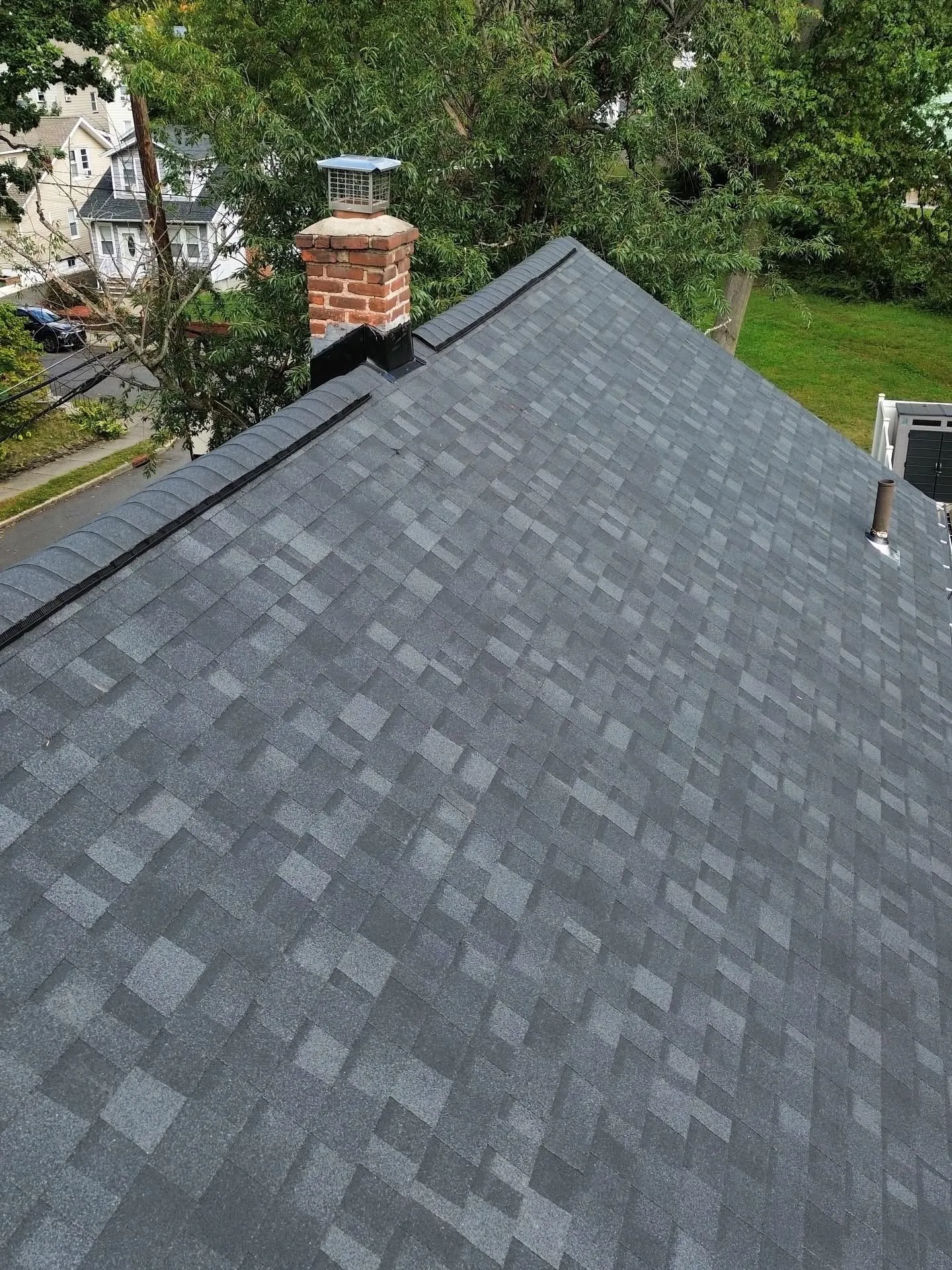 Close-up of a repaired brick chimney with new stainless cap and fresh black flashing on a new gray roof