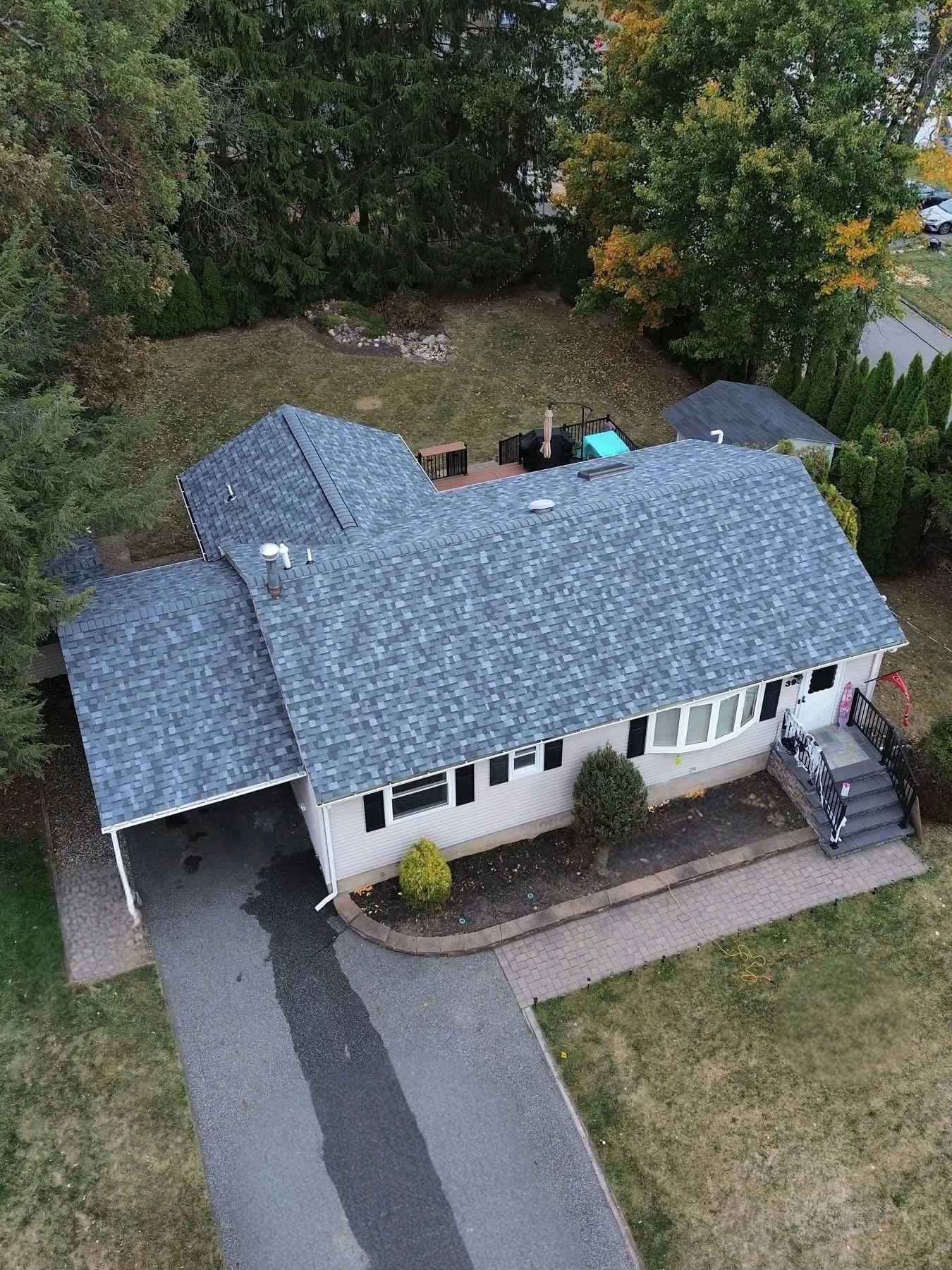 Drone view of a completed gray architectural shingle roof replacement on a ranch home with carport