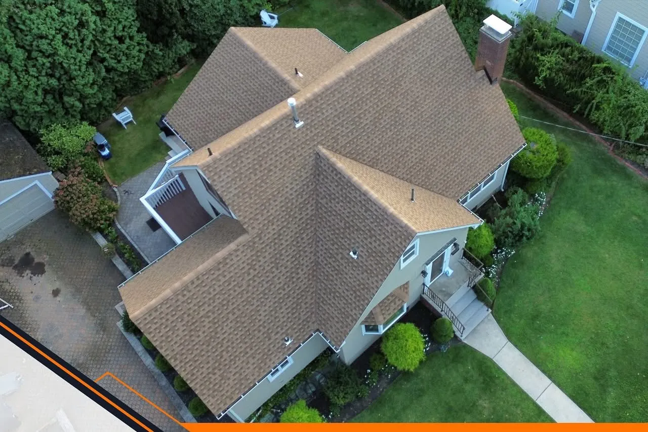 Aerial view of a large completed tan shingle roof on a colonial with brick chimney and landscaped yard