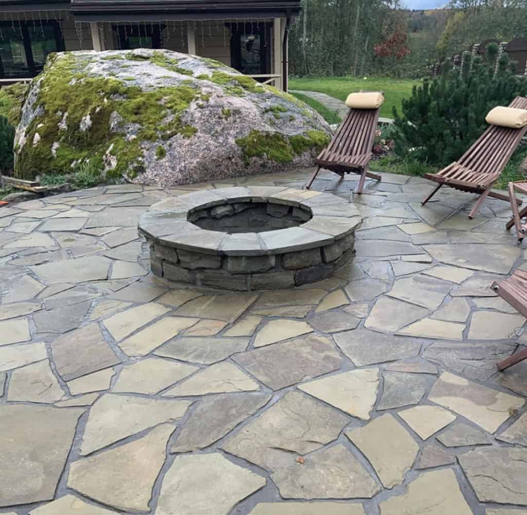 An outdoor patio with a stone fire pit and wooden lounge chairs.